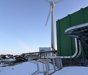 A ladder lying on its side in the snow, behind a green building and with the station wind turbine in the background