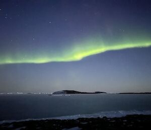 A band of green aurora stretched across a dark blue sky, with rocky islands in the distance and an ice sea in the foreground