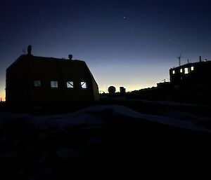 The silhouette of two dark buildings with glowing windows stands out against a blue night sky