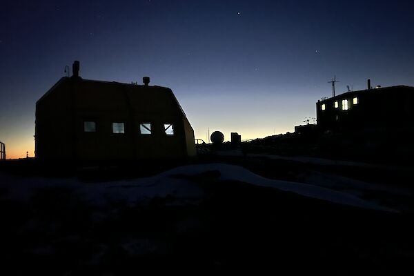 The silhouette of two dark buildings with glowing windows stands out against a blue night sky