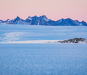a picture from the sea ice, showing a full moon just above the horizon, with jagged mountains and icy coastline in background