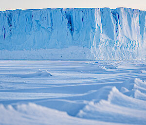 A ground-level photo of a snow and ice trail leading to a tabular iceberg in the background.