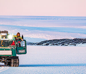 Four expeditioners in an over-snow tracked Hagglands vehicle, waving to the camera while travelling on the sea ice.