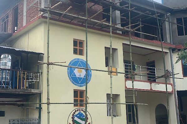 An existing white building in Nepal of two stories has scaffolding to support the construction of two newfloors above