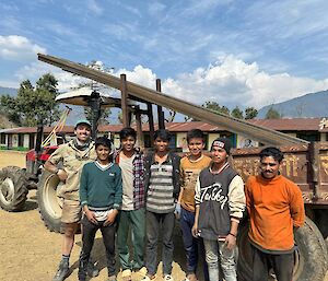 A man wearing constriction clothes stands with a group of youn Nepalese boys in front of a truck holding construction materials