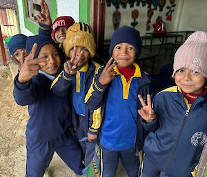 6 young Nepalese children wearing a blue and yellow school uniform pose smiling in the doorway of a classroom