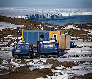 A blue hagglands parked in front of a hut with a view to a glacier and a bay behind.