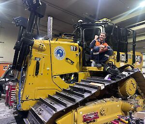 A man sitting in the cab of a bulldozer, inside a workshop.