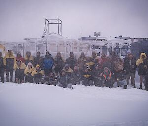 The Casey winter team photo - a group of people sitting on the snow and some standing behind.