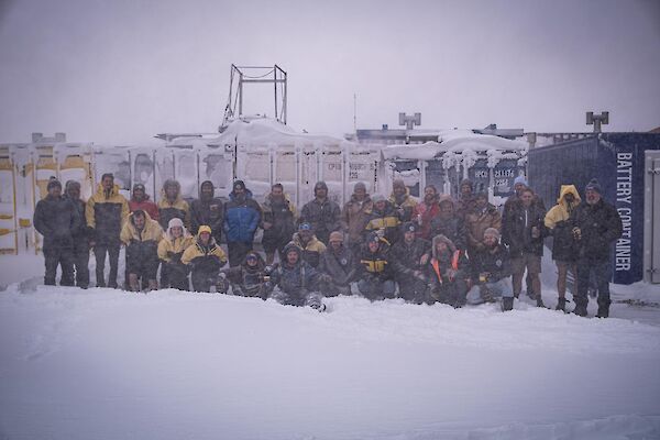 The Casey winter team photo - a group of people sitting on the snow and some standing behind.