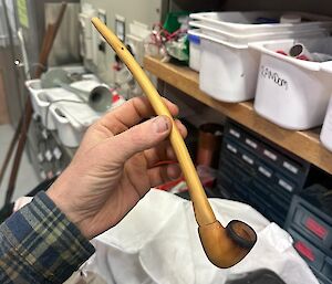 A hand holding a long wooden pipe.