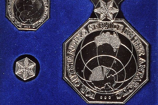 A metal medal showing Australia and Antarctica, on a white and blue ribbon, on a royal blue background