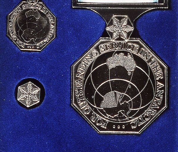 A metal medal showing Australia and Antarctica, on a white and blue ribbon, on a royal blue background