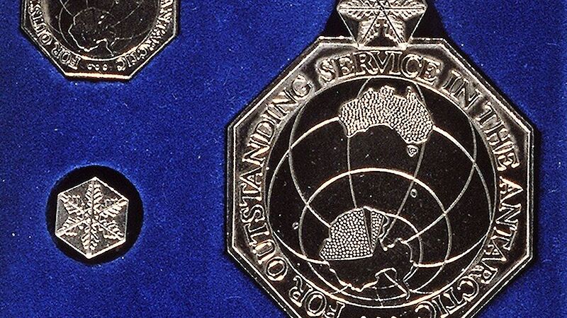 A metal medal showing Australia and Antarctica, on a white and blue ribbon, on a royal blue background