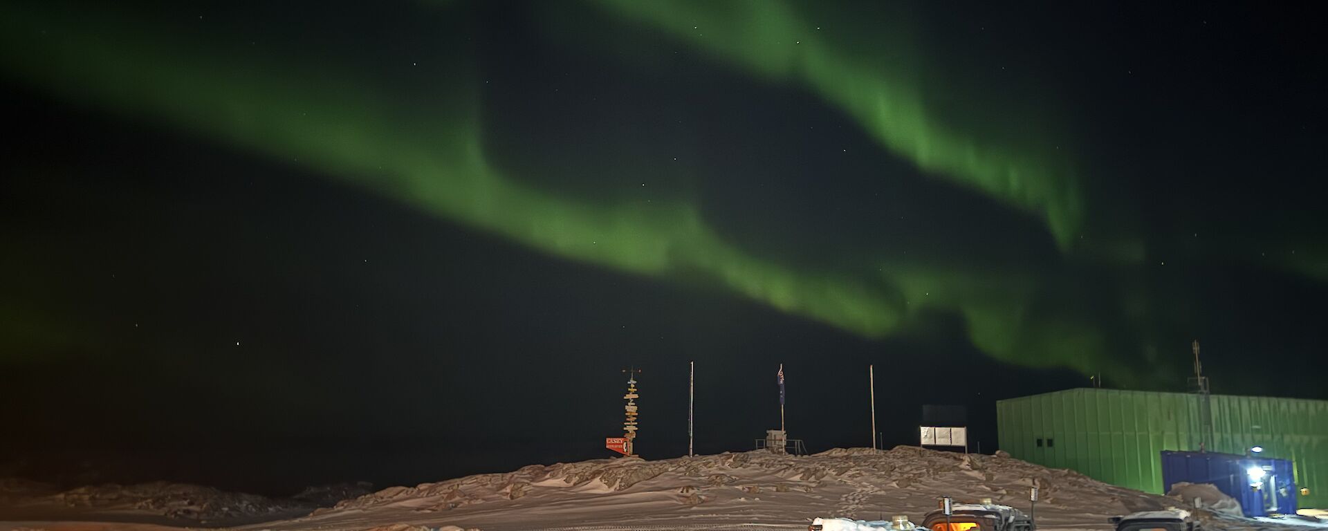 A green aurora in the sky above some parked Polaris vehicles and a green shed.