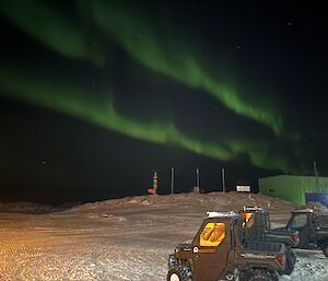 A green aurora in the sky above some parked Polaris vehicles and a green shed.