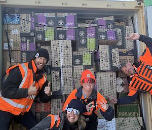 Four people posing in front of a shipping container filled with food supplies.