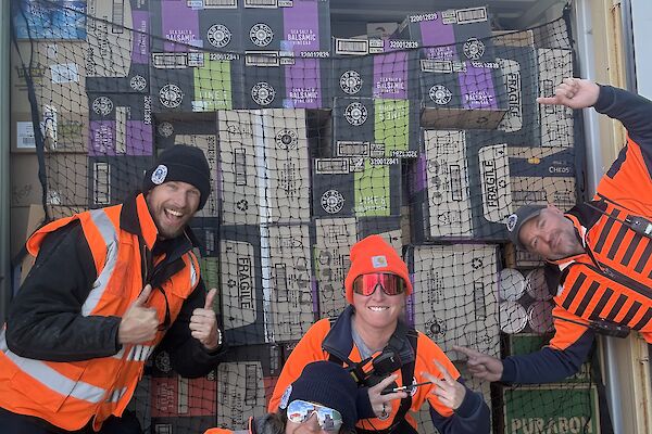 Four people posing in front of a shipping container filled with food supplies.