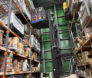 A forklift lifting a pallet of coffee from a high row of shelves.
