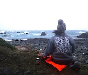 A woman sitting on an orange jacket looking over a beach.
