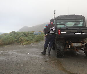 A woman leaning against a Polaris vehicle looking at the view of mountains and a Macquarie Island sign.
