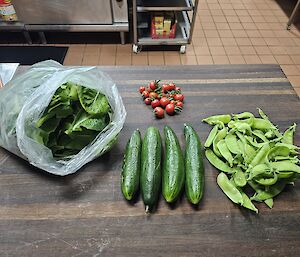 A picture of lettuce, cucumbers, red tomatoes and snow peas on a chopping board in the kitchen