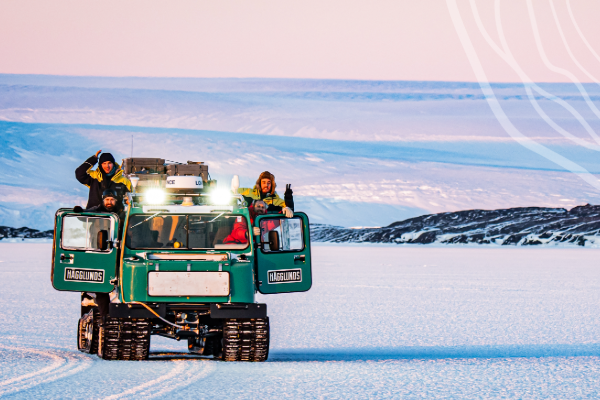 Four people in a green hagglund parked on sea ice, with an ice plateau rising behind.