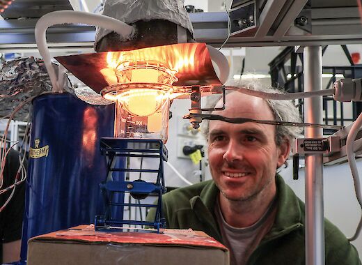 A man looking at ice in a glass beaker on a tripod. The ice is being converted from a solid to a gas in a vaccuum.