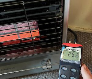 A multimeter, displaying 2.52 on the screen is held in front of an old style gas heater