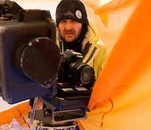A man inside a yellow bag looking at a monitoring camera.
