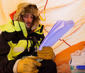 A man reading an instruction manual for a camera inside a lightweight bag to keep snow off.