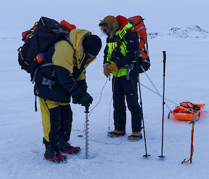 Two people testing the thickness of sea ice with a hand-held drill.