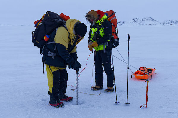 Two people testing the thickness of sea ice with a hand-held drill.
