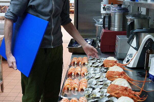 An expeditioner surveys the array of seafood being plated up in the kitchen.