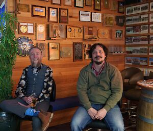 Two expeditioners sitting at a table in the bar area, surrounded by photos on the wall behind.