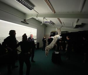 People in a darkened room gathered around an albatross model that is hanging from the ceiling.