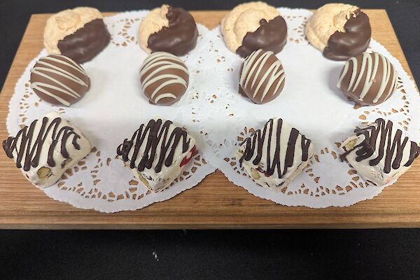 A wooden platter with paper doilies presents 12 petit four sweets.