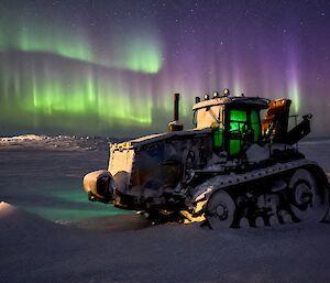 A snow-covered tractor with a green and purple aurora in the sky.