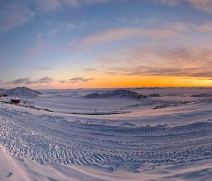 A panoramic photo of an orange sunrise. Snow coverd in tractor tyre marks are visible at the front of the photo.