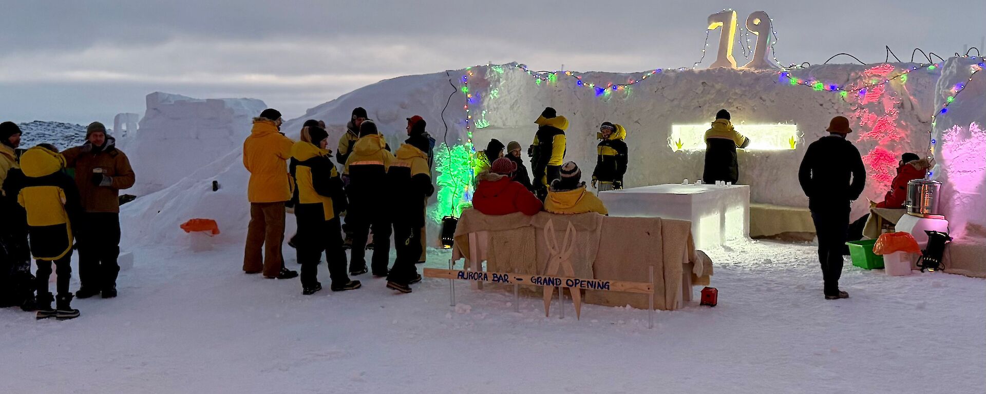 People gathering around a colourfully lit bar with walls build from blocks of ice.