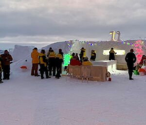People gathering around a colourfully lit bar with walls build from blocks of ice.