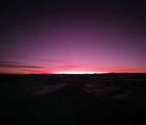 A glowing pink sunset stretched into a deep purple sky above a dark snowy landscape.