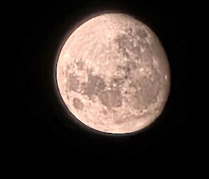 An almost full moon is clear in a very dark sky with no stars visible in the picture.