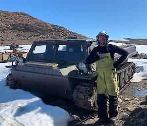 A man standing in front of an old Russion vehicle, surrounded by melting snow.