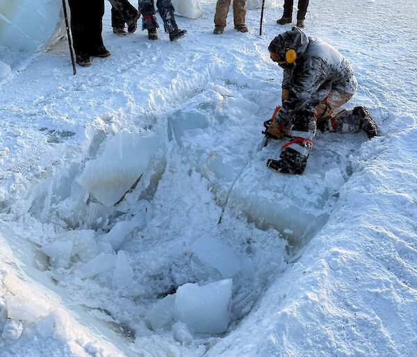 An expeditioner using a chainsaw to prepare cutting a square hole into the sea ice