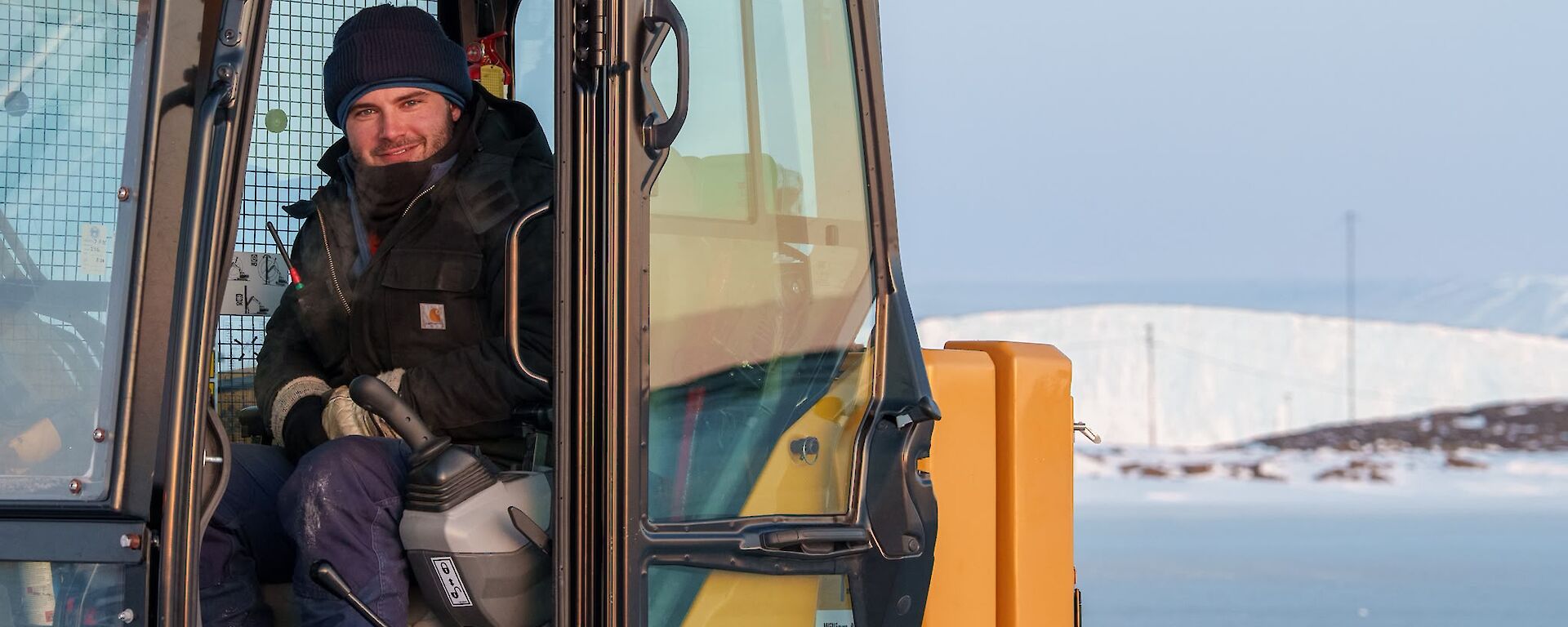 An expeditioner sitting in an excavator, ready to remove large blocks of ice from the sea-ice swimming hole