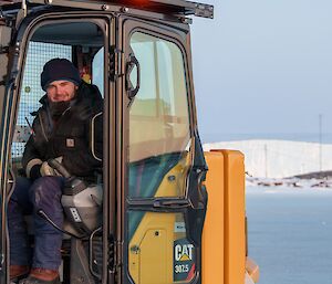 An expeditioner sitting in an excavator, ready to remove large blocks of ice from the sea-ice swimming hole