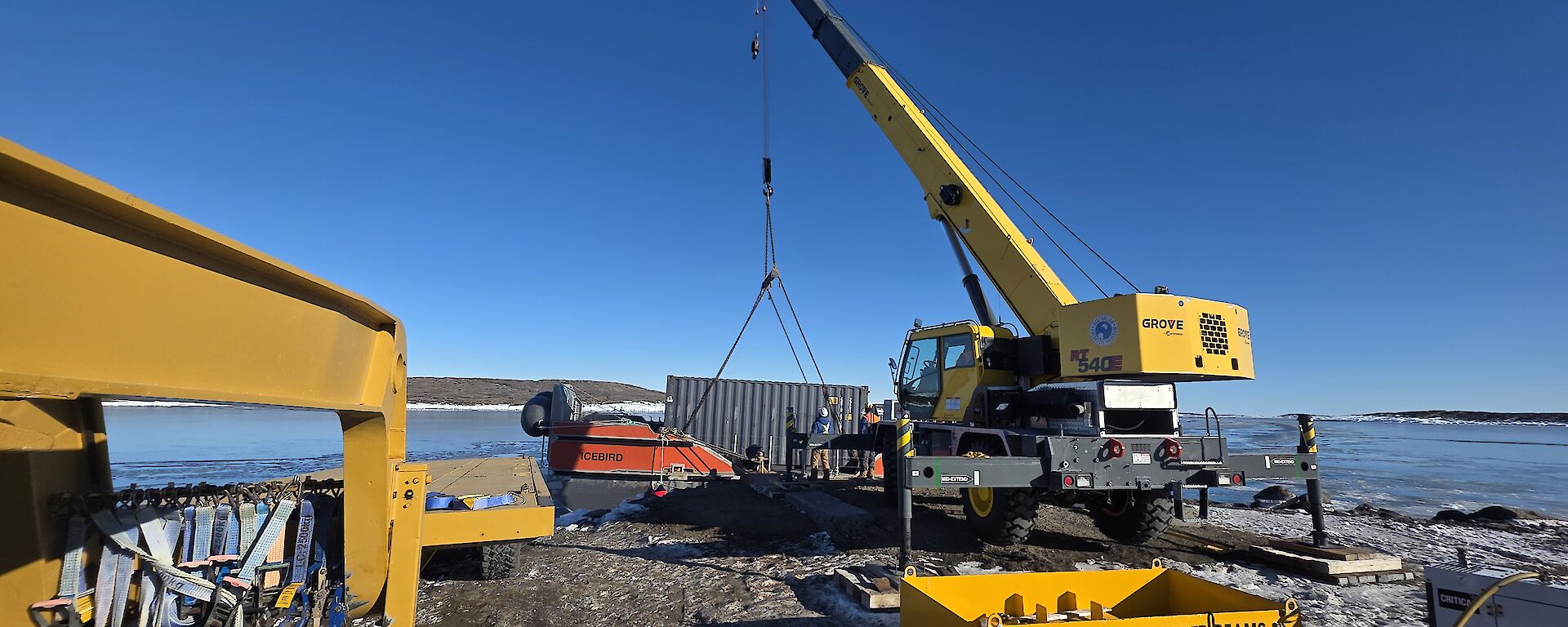 A large yellow crane is lifting a red watercraft onto a wharf