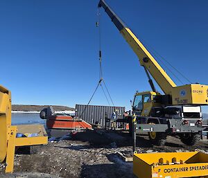 A large yellow crane is lifting a red watercraft onto a wharf
