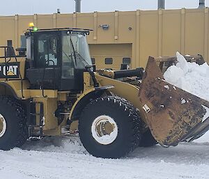 A yellow bulldozer is carrying a bucket filled with snow